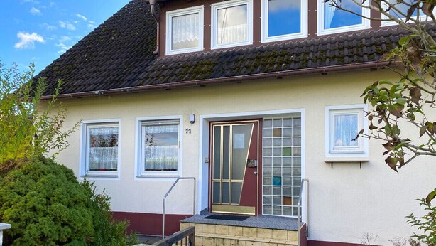Ein zweistöckiges Haus mit Ziegeldach, einer Haustür mit Glasfenstern und der Hausnummer 11 an der Wand.