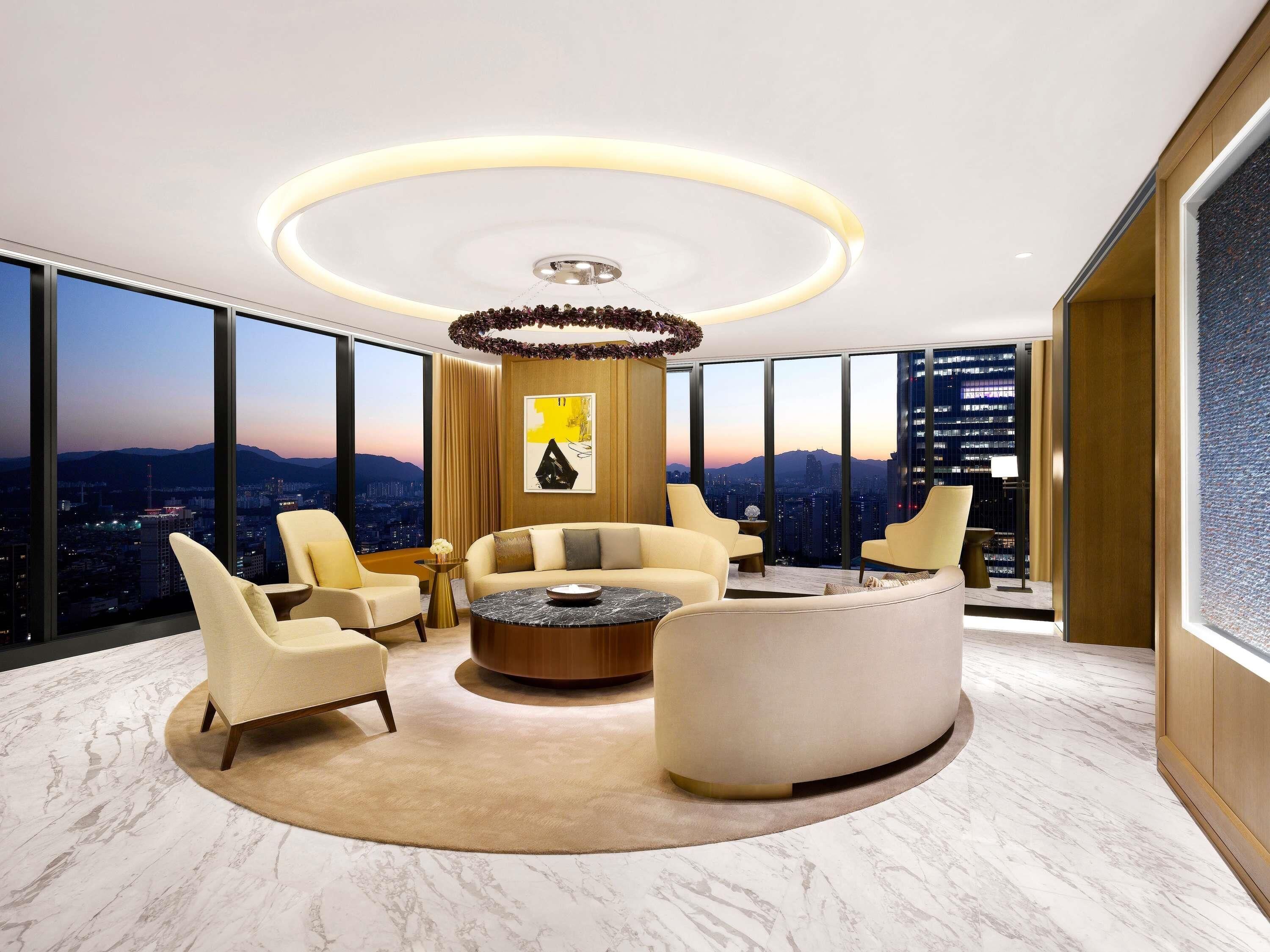 Un salon moderne avec vue sur la ville, comprenant une table basse ronde, deux canapés et une grande fenêtre.