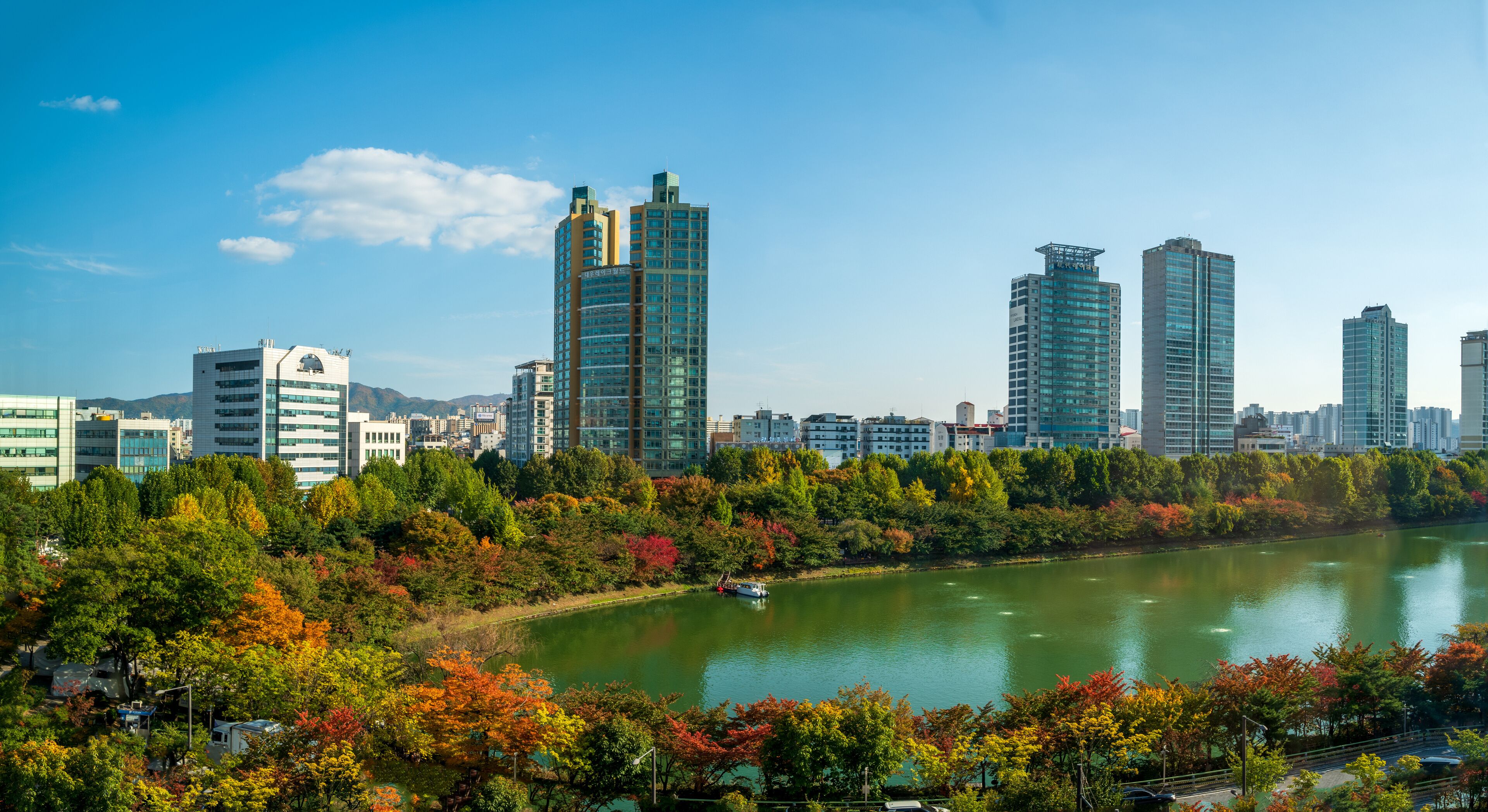 A cityscape with modern high-rise buildings, a river, and autumn foliage.
