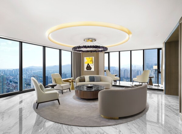 Un interior de rascacielos con una zona de estar moderna, que incluye un sofá, sillones, una mesa de centro y vistas a la ciudad.
