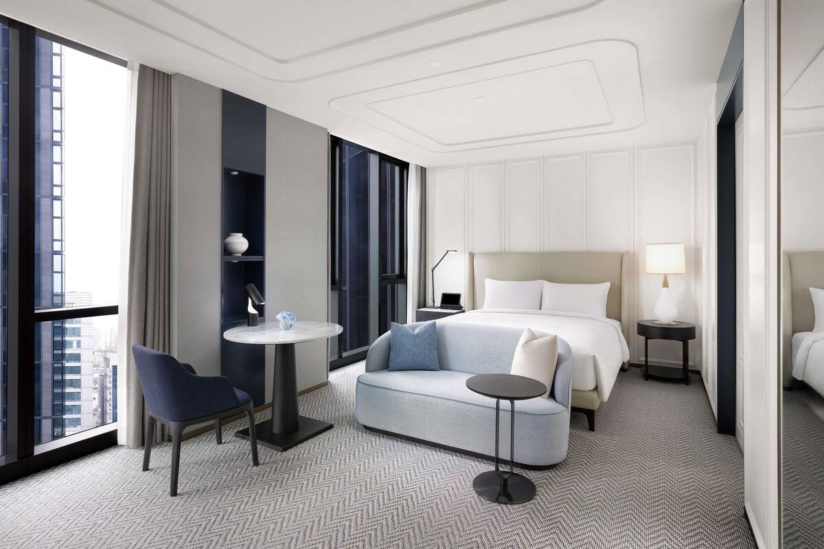 Una habitación de hotel moderna con una cama grande, una mesa redonda, un sofá y una silla.