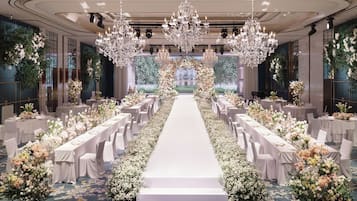A formal event space with a central aisle, chandeliers, floral arrangements, and tables set for a reception.