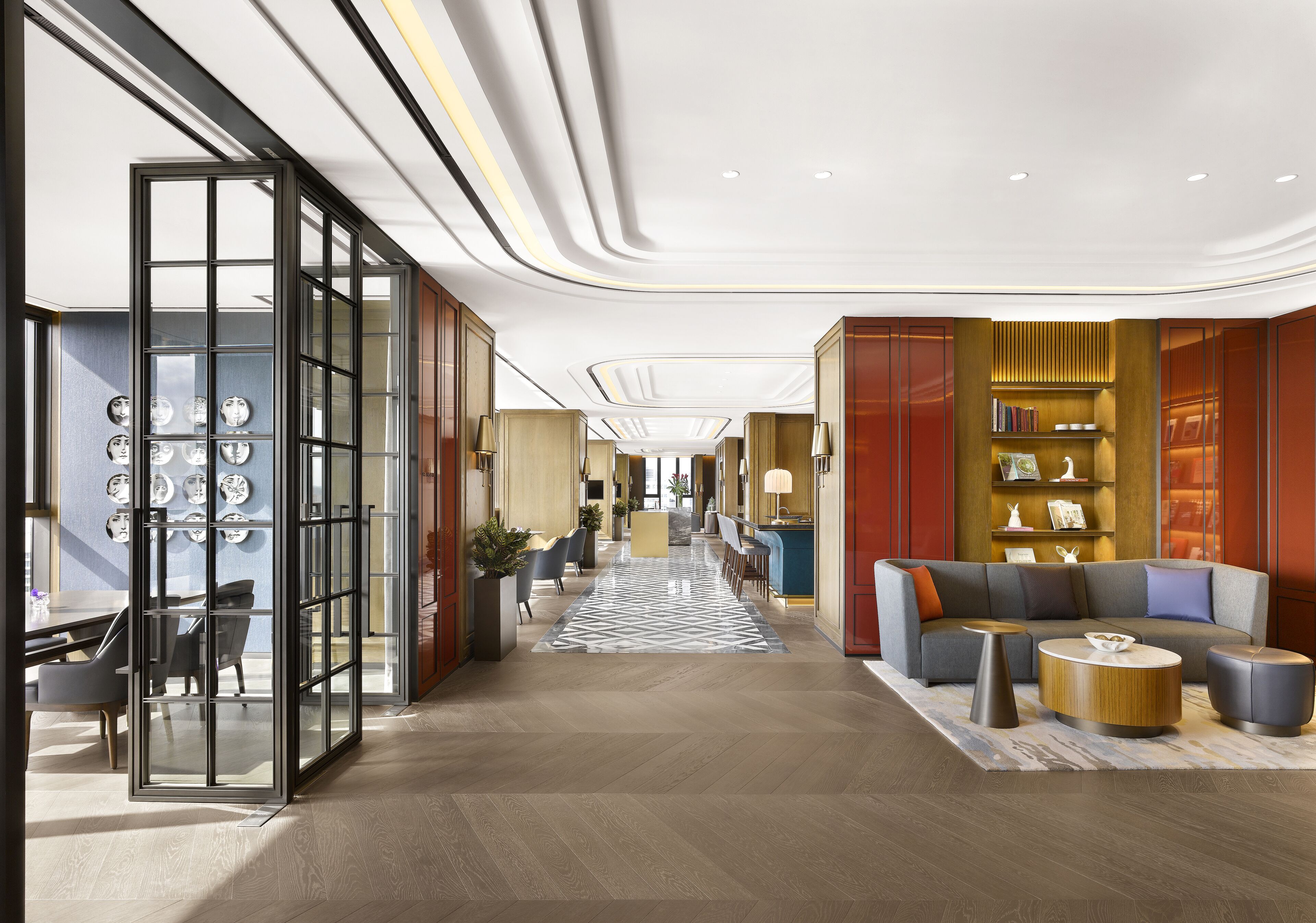 Una hall d'hotel moderna con un'area salotto centrale, una reception e un divisorio in vetro decorato con piatti.