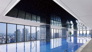 Une piscine intérieure moderne avec vue sur la ville, de grandes fenêtres et un design de plafond unique.