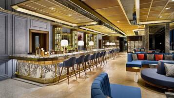 A bar area with a marble countertop, bar stools, and a seating area with sofas and chairs.