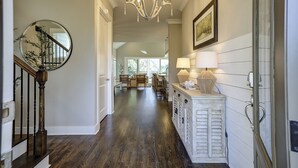 A hallway with a wooden staircase, a chandelier, a mirror, and a dining area in the background. - 13 Starboard Tack - Beautiful oasis w/ private dock & Pool - Sleeps up to 17 (Hilton Head Island)
