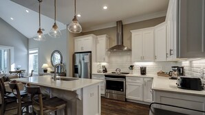 A modern kitchen with white cabinetry, stainless steel appliances, and a central island with bar stools. - 13 Starboard Tack - Beautiful oasis w/ private dock & Pool - Sleeps up to 17 (Hilton Head Island)