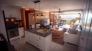 A modern kitchen with white cabinets, a central island, and a dining area with a white sofa and a view of the outdoors. - 4 Dolphin views La Mercy (La Mercy)