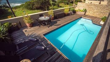 A wooden deck with a pool, lounge chairs, and a table with chairs.