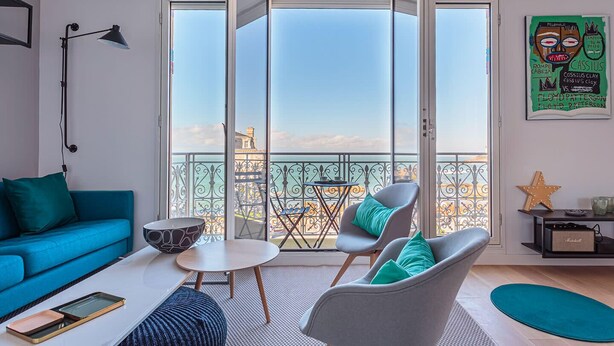 A modern living room with a blue sofa, grey armchairs, a small table, and a balcony with a view of the city. - ALTAYA • Apt with balcony and sea view in Biarritz (Biarritz)
