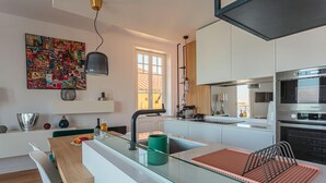 A modern kitchen with a central island, a dining area with a wooden table, and a colorful abstract art piece on the wall. - ALTAYA • Apt with balcony and sea view in Biarritz (Biarritz)