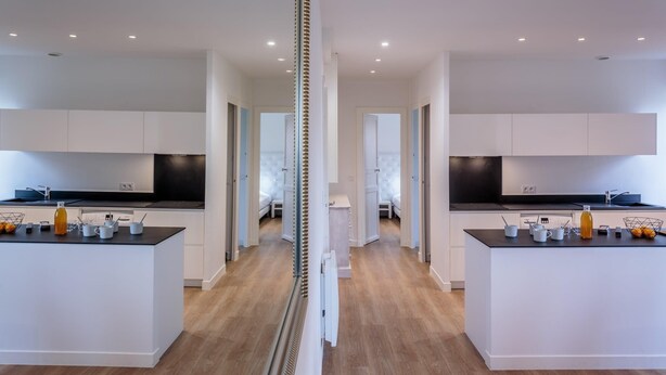 Une cuisine moderne dotée de deux îlots, de meubles blancs et d’un passage central.