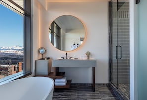 A modern bathroom with a large round mirror, a bathtub, and a shower area.