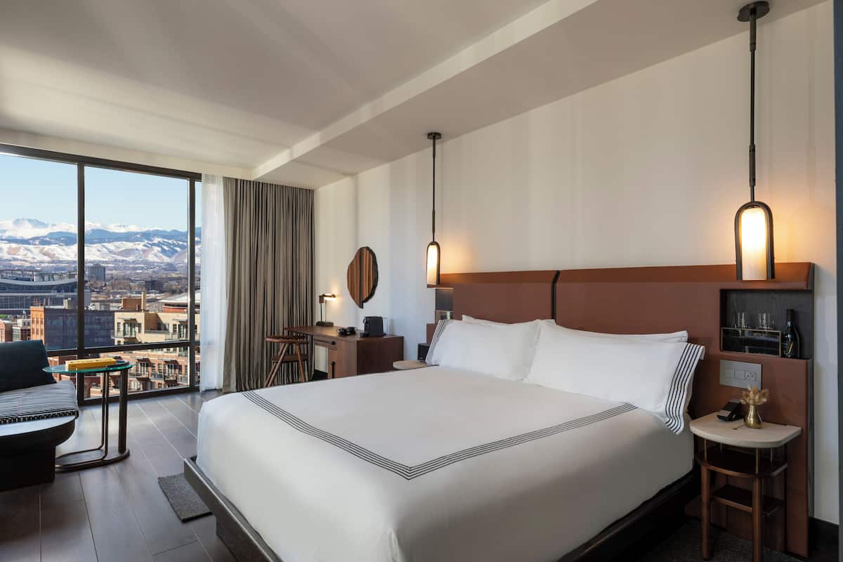 Ein Hotelzimmer mit einem großen Bett, einem Schreibtisch, einem Stuhl und Blick auf eine Stadtlandschaft.