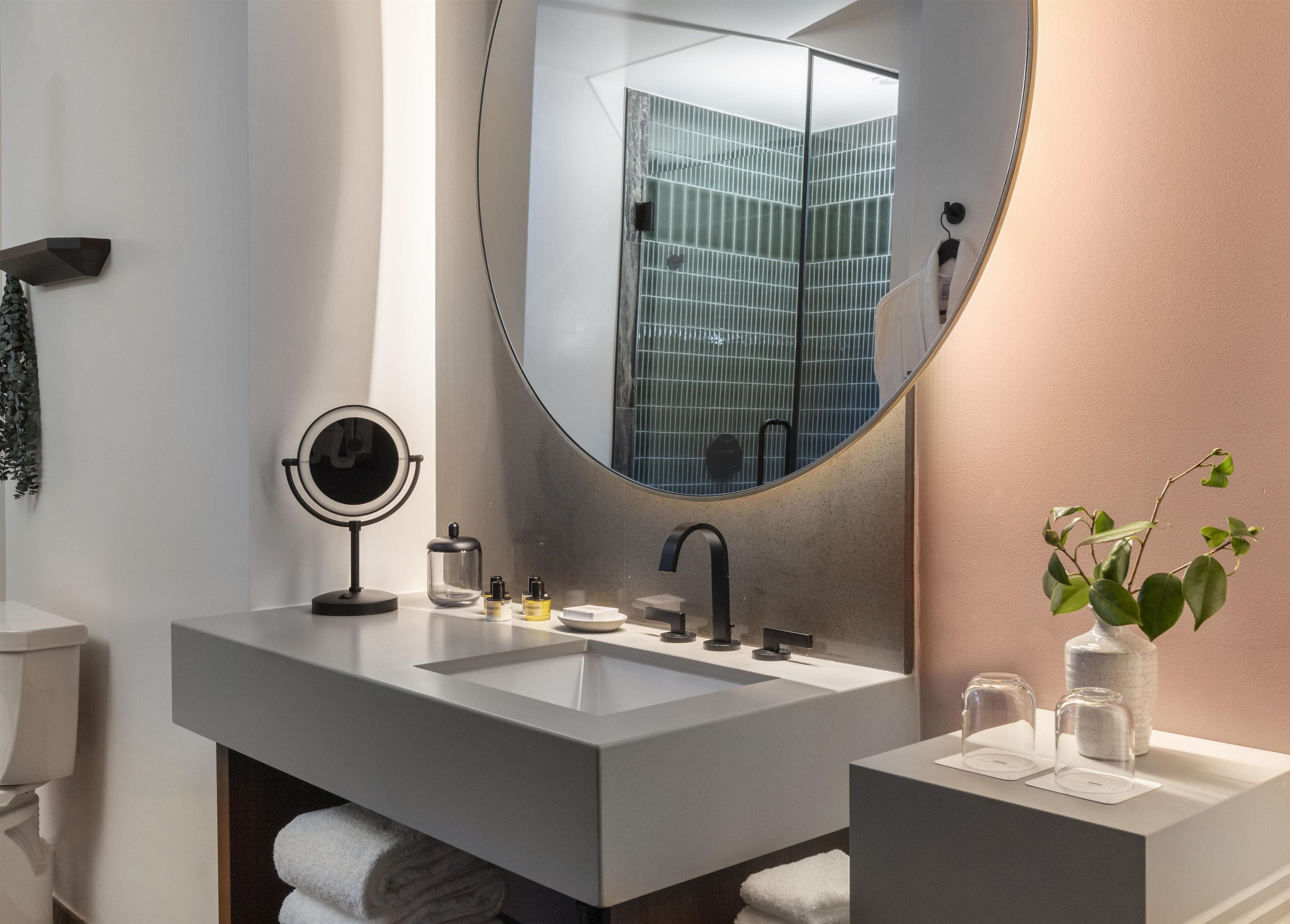 Un baño moderno con un espejo grande, dos lavamanos, un espejo redondo y un florero con una planta.