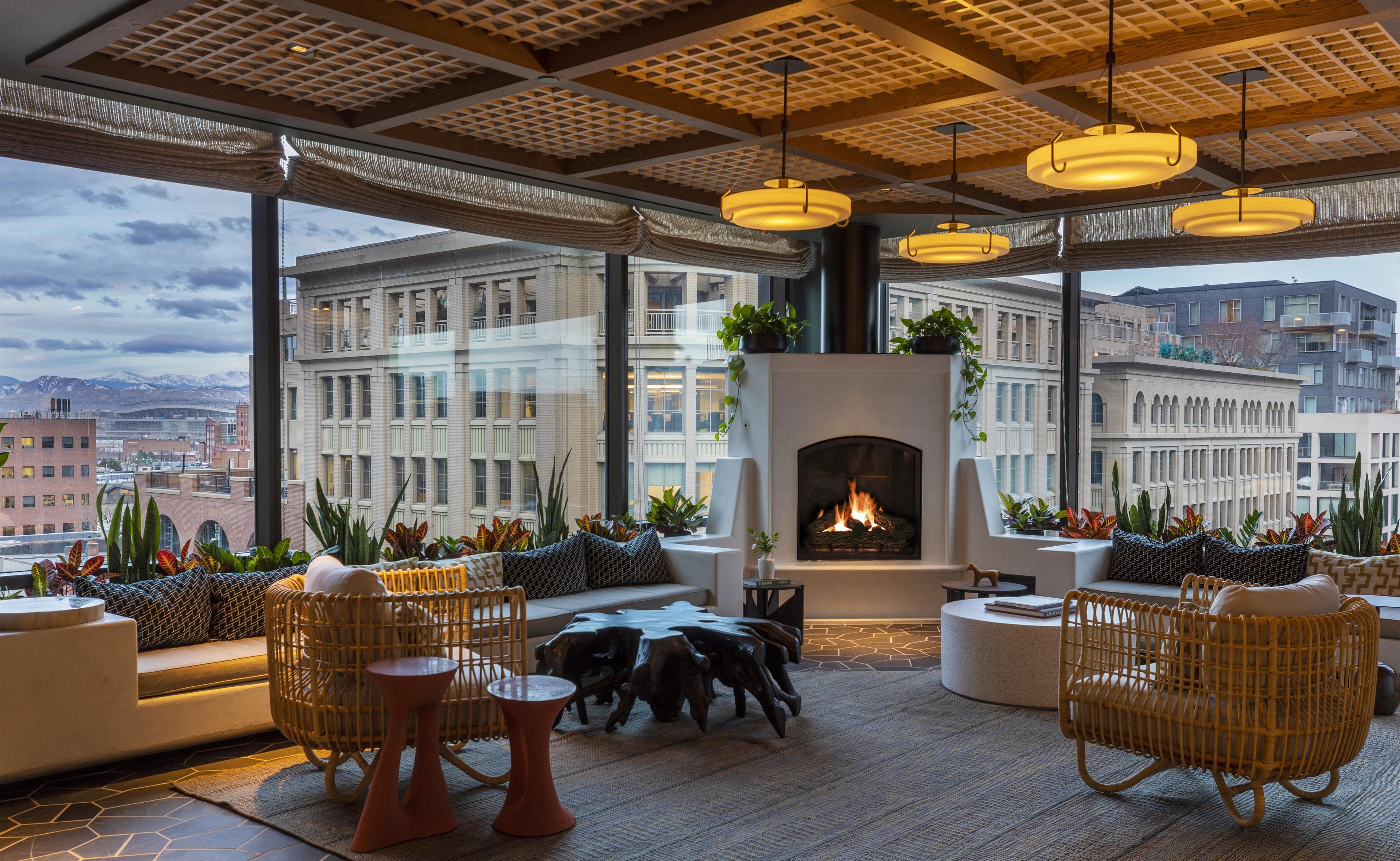 A modern lounge with a fireplace, wicker furniture, and a view of the cityscape.