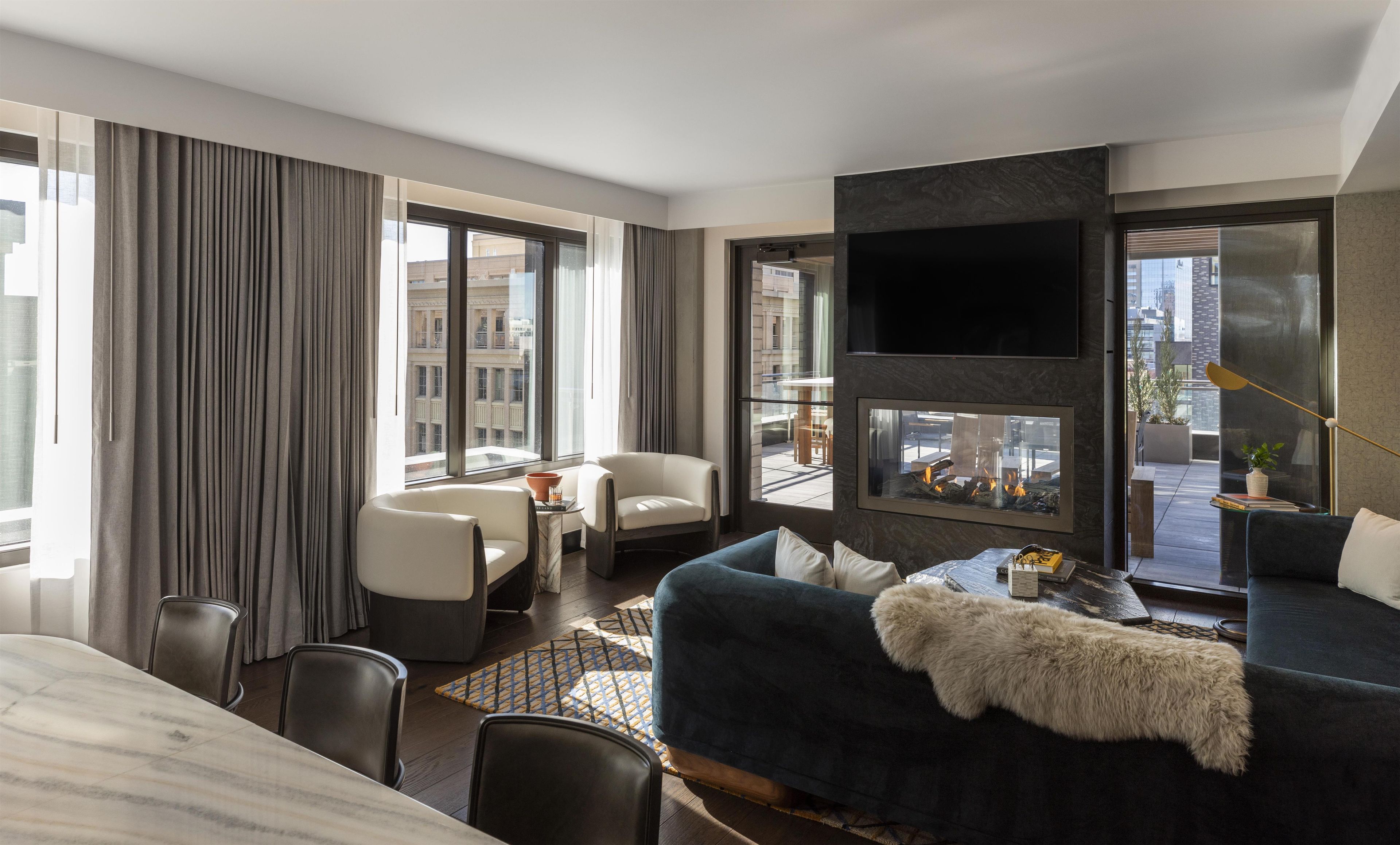 A modern hotel room with a large window, a flat-screen TV, a fireplace, and a cozy seating area.