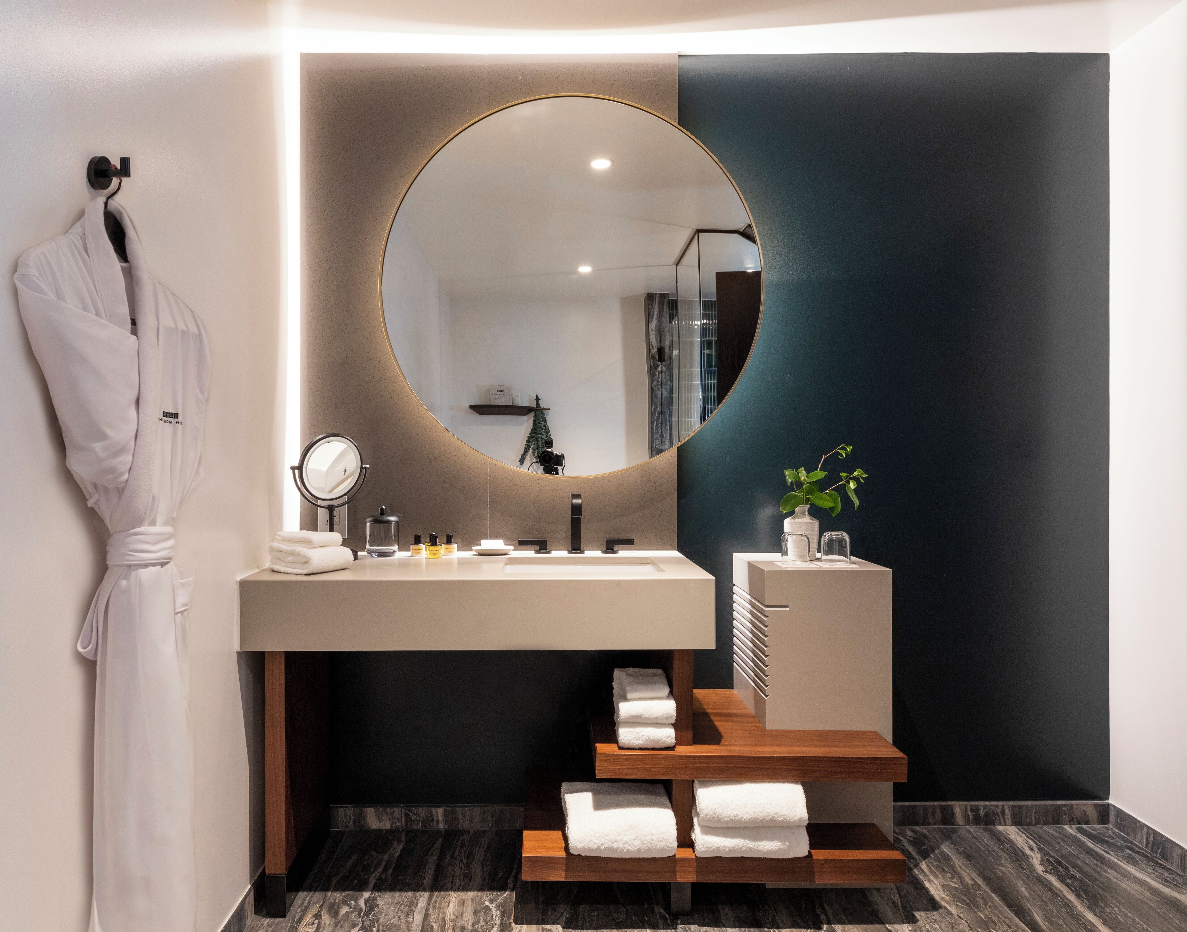 A modern bathroom with a round mirror, a sink, and a wooden towel rack.