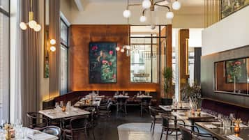 A restaurant with multiple dining tables, chairs, and a large painting on the wall.