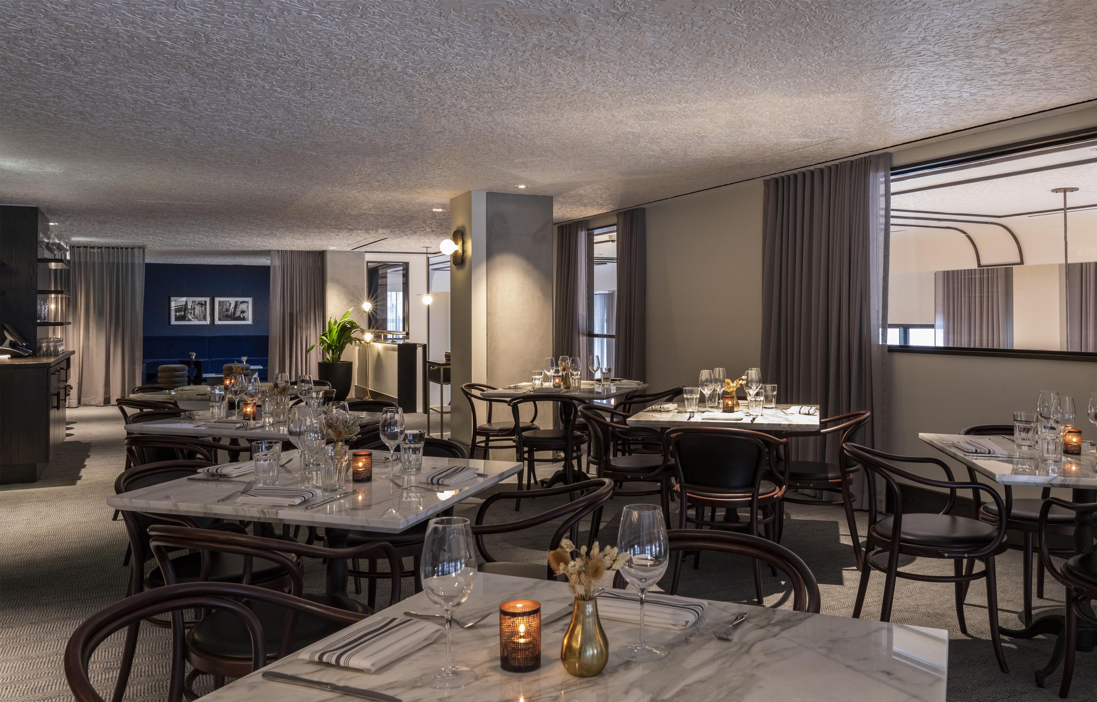 Een restaurant met meerdere tafels gedekt voor diners, met marmeren tafels en donkere stoelen.