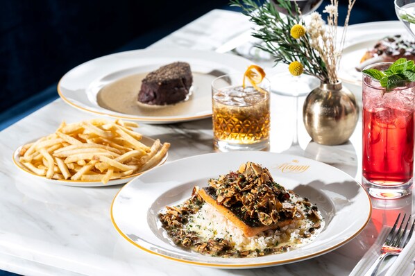 A dining table with plates of food, including a fish dish, fries, and a dessert. There are also glasses of beverages and a vase with flowers.