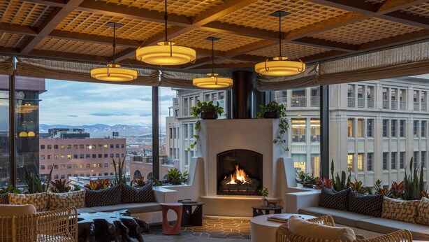A modern lounge area with wicker furniture, a fireplace, and large windows offering city views. - Thompson Denver, by Hyatt (Denver)