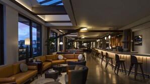 A modern lounge area with a bar, seating arrangements, and large windows offering views of the cityscape. - Thompson Denver, by Hyatt (Denver)