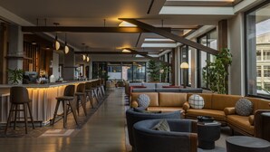 A modern bar area with seating and a bar counter, large windows, and indoor plants. - Thompson Denver, by Hyatt (Denver)