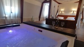 A room with a large bathtub, a wooden bench, and a bedside table with a bottle and glasses. - Très Grand Loft Sous Les Toits - Château La Vidalle (Vendres)