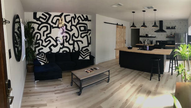 A modern living room with a black sofa, a coffee table, and a kitchen area with a wooden island, pendant lights, and a black refrigerator. - 2BR Lit & Spacious Across from Netflix (Los Angeles)