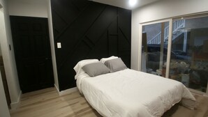 A bedroom with a bed, two pillows, a black geometric wall, a sliding glass door, and a wooden floor. - 2BR Lit & Spacious Across from Netflix (Los Angeles)