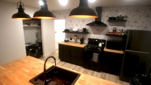 A modern kitchen with a wooden countertop, black cabinets, and pendant lighting. - 2BR Lit & Spacious Across from Netflix (Los Angeles)
