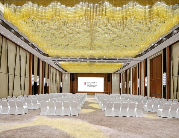 A conference room with rows of white chairs, a large screen, and a decorative golden chandelier. - Hualuxe Suzhou Bay Hot Spring Resort, an IHG Hotel (Suzhou)