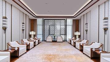 A hotel room with a large, patterned carpet, a central seating area with chairs and tables, and a decorative wall panel.