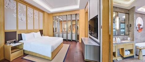 A modern hotel room with a large bed, a TV, a bathroom with a mirror, and a wooden floor.