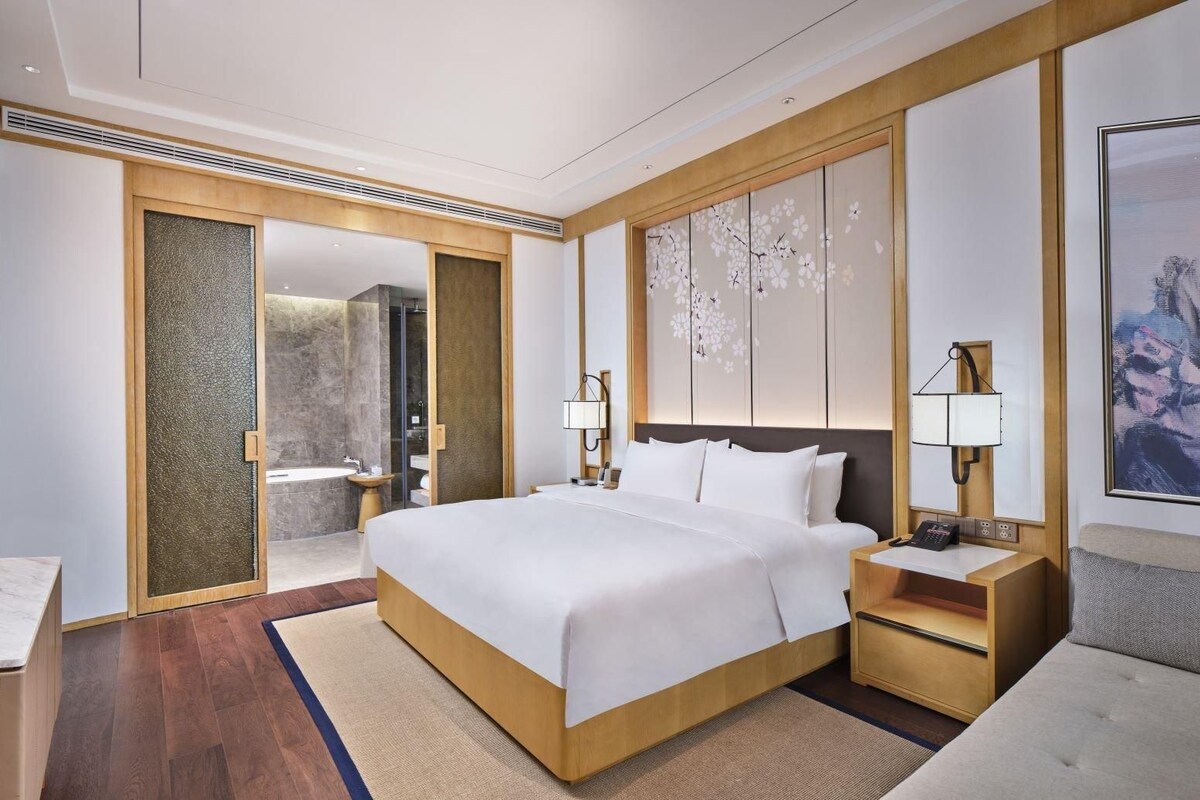 A modern hotel room with a large bed, a TV, a bathroom with a bathtub, and a shower.