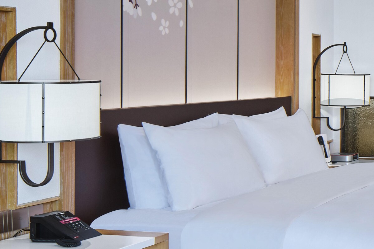 A hotel room with a bed, bedside lamps, a telephone, and a wall with a floral design.