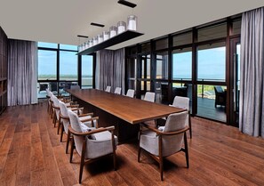 A conference room with a long wooden table, grey upholstered chairs, and large windows offering a view of the sea. - Hualuxe Suzhou Bay Hot Spring Resort, an IHG Hotel (Suzhou)