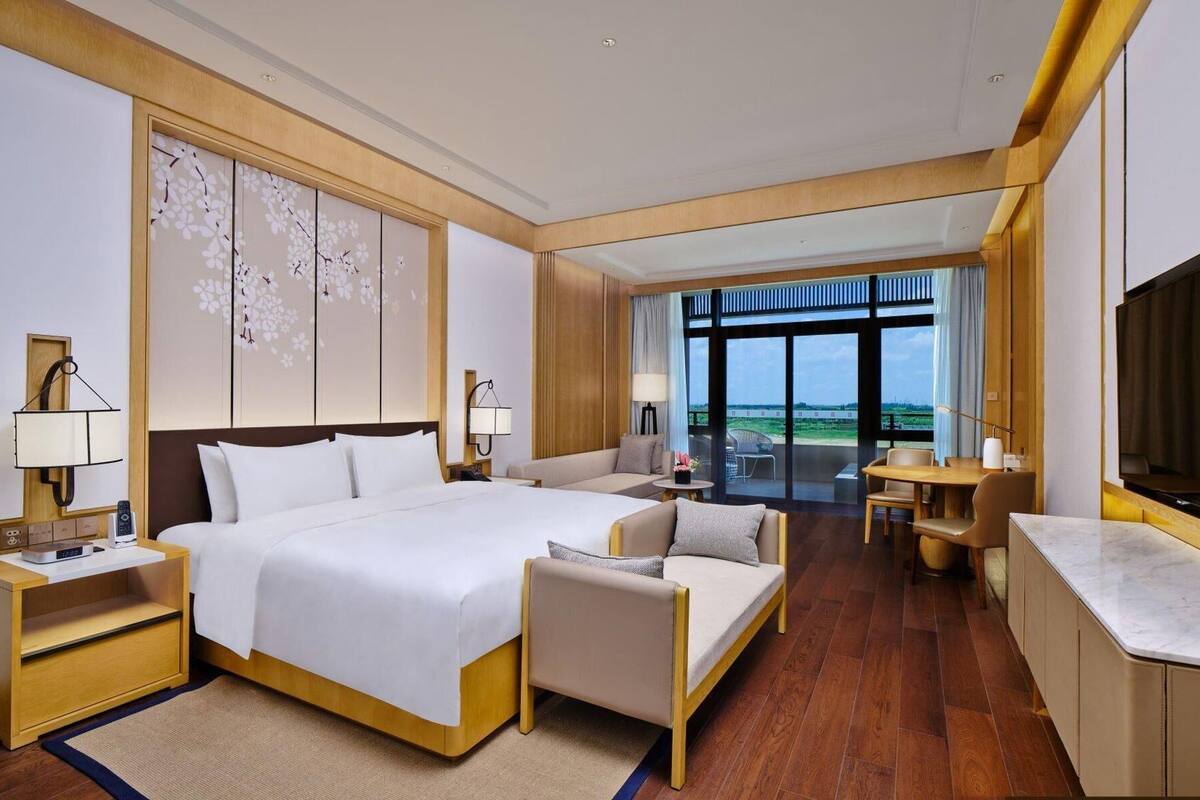 A hotel room with a large bed, a sofa, a TV, and a view of the outdoors.