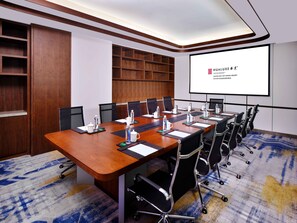 A conference room with a long table, chairs, a projector screen, and a wooden panel wall. - Hualuxe Suzhou Bay Hot Spring Resort, an IHG Hotel (Suzhou)