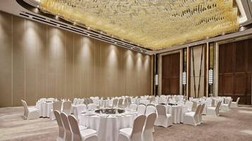 A conference room with round tables, white chairs, and a large chandelier.