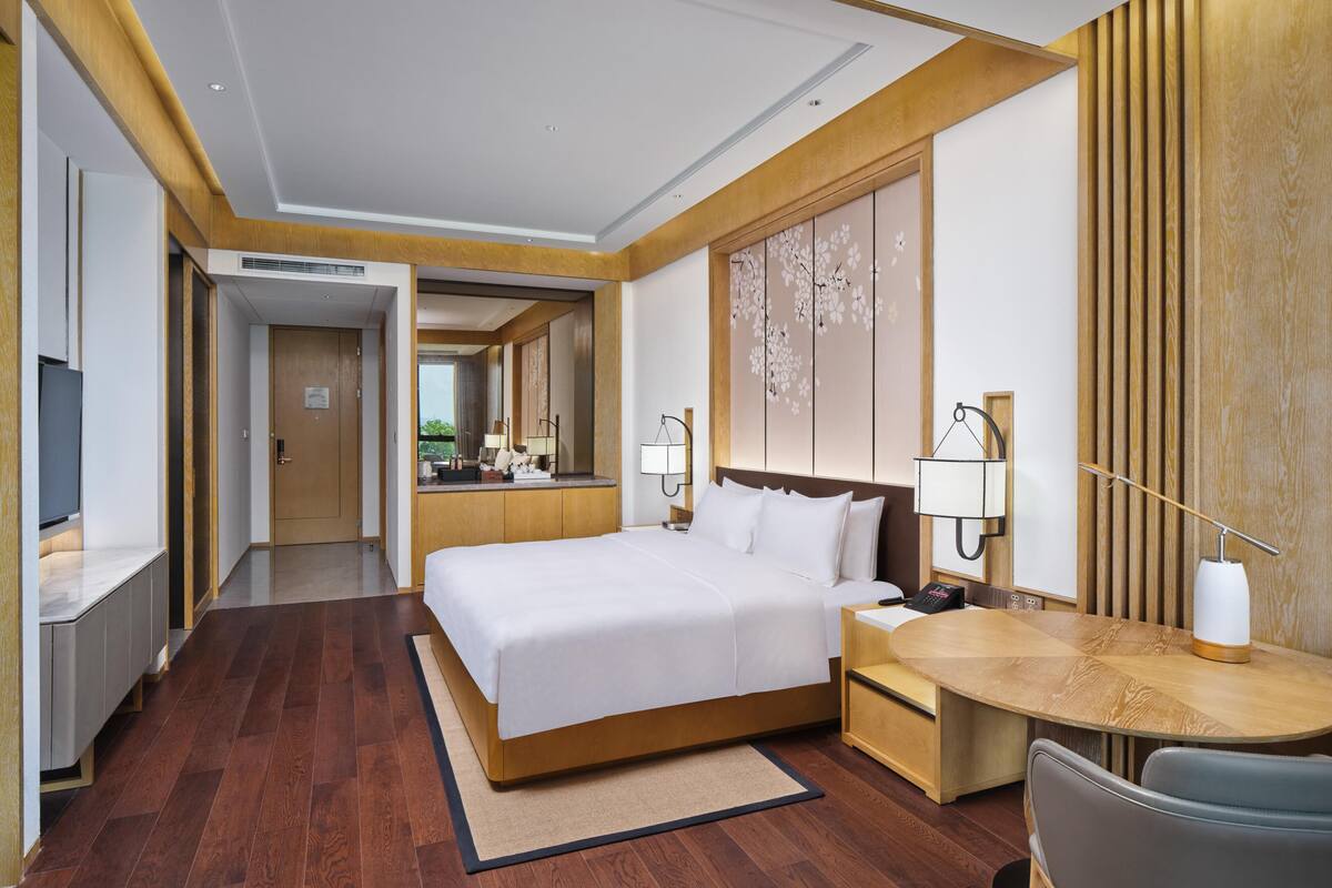 A hotel room with a bed, desk, chair, and a large mirror.