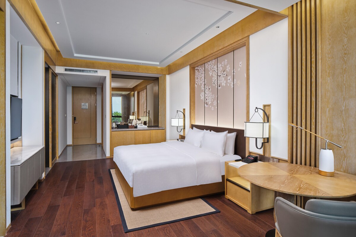 A hotel room with a bed, desk, chair, and a large mirror.