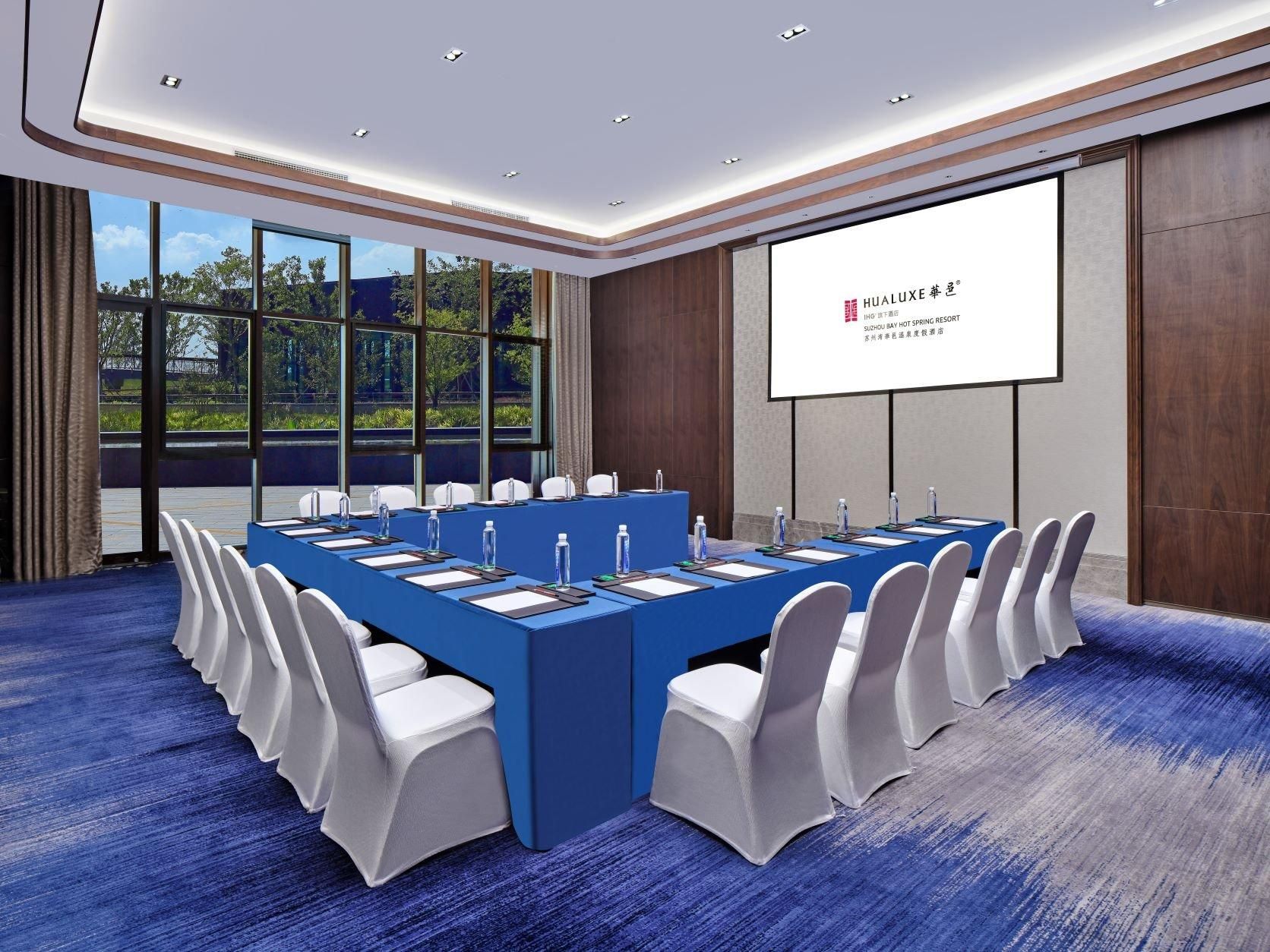 A conference room with a long table, white chairs, and a projector screen.