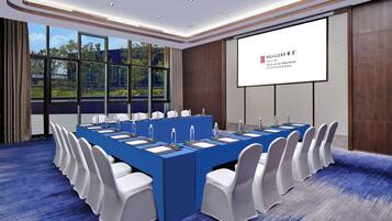 A conference room with a long table, white chairs, and a projector screen.