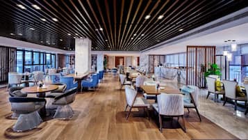 Un'ampia sala da ristorante con pavimento in legno, arredamento moderno e grandi finestre che offrono una vista.