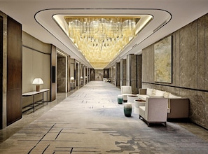 Un pasillo moderno de hotel con techo alto, candelabros, zonas de estar y obras de arte en las paredes.