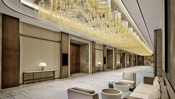 A hotel lobby with a long corridor, seating areas, and a decorative ceiling light fixture.