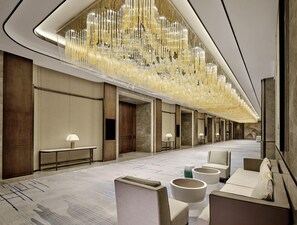 A hotel lobby with a long corridor, seating areas, and a decorative ceiling light fixture. - Hualuxe Suzhou Bay Hot Spring Resort, an IHG Hotel (Suzhou)