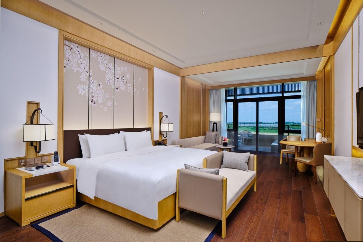 A hotel room with a bed, a sofa, a TV, and a view of the outdoors.
